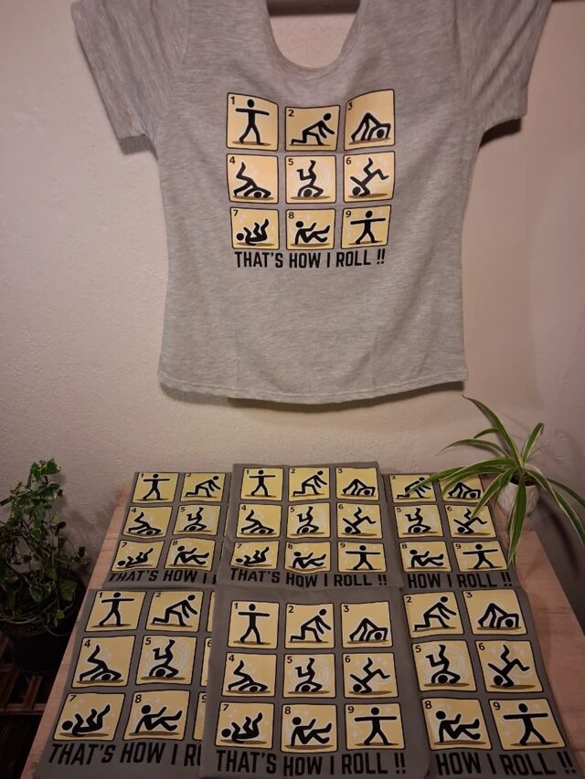 A grey "That's How I Roll" shirt on the wall above a table of printed transfers