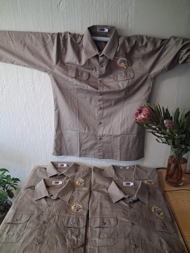 Embroidered Savannah Safaries bush shirts, one hanging on a wall and four on a table